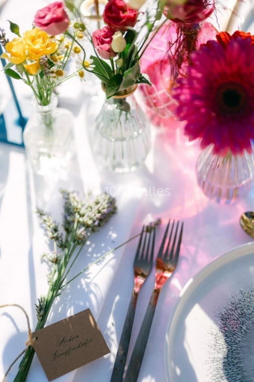 Bouquet de fleurs colorées dans des vases en verre sur une table décorée avec couverts, assiette et carte en papier.