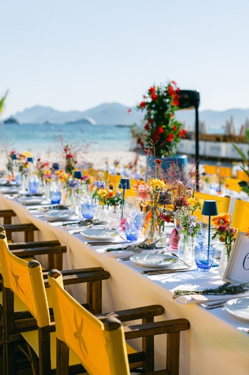 Table dressée en extérieur avec nappes blanches, chaises jaunes et décorations florales, en bord de plage.