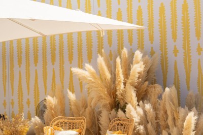 Chaises en rotin entourées de pampas et de décorations jaunes, sous un parasol blanc dans un cadre lumineux.