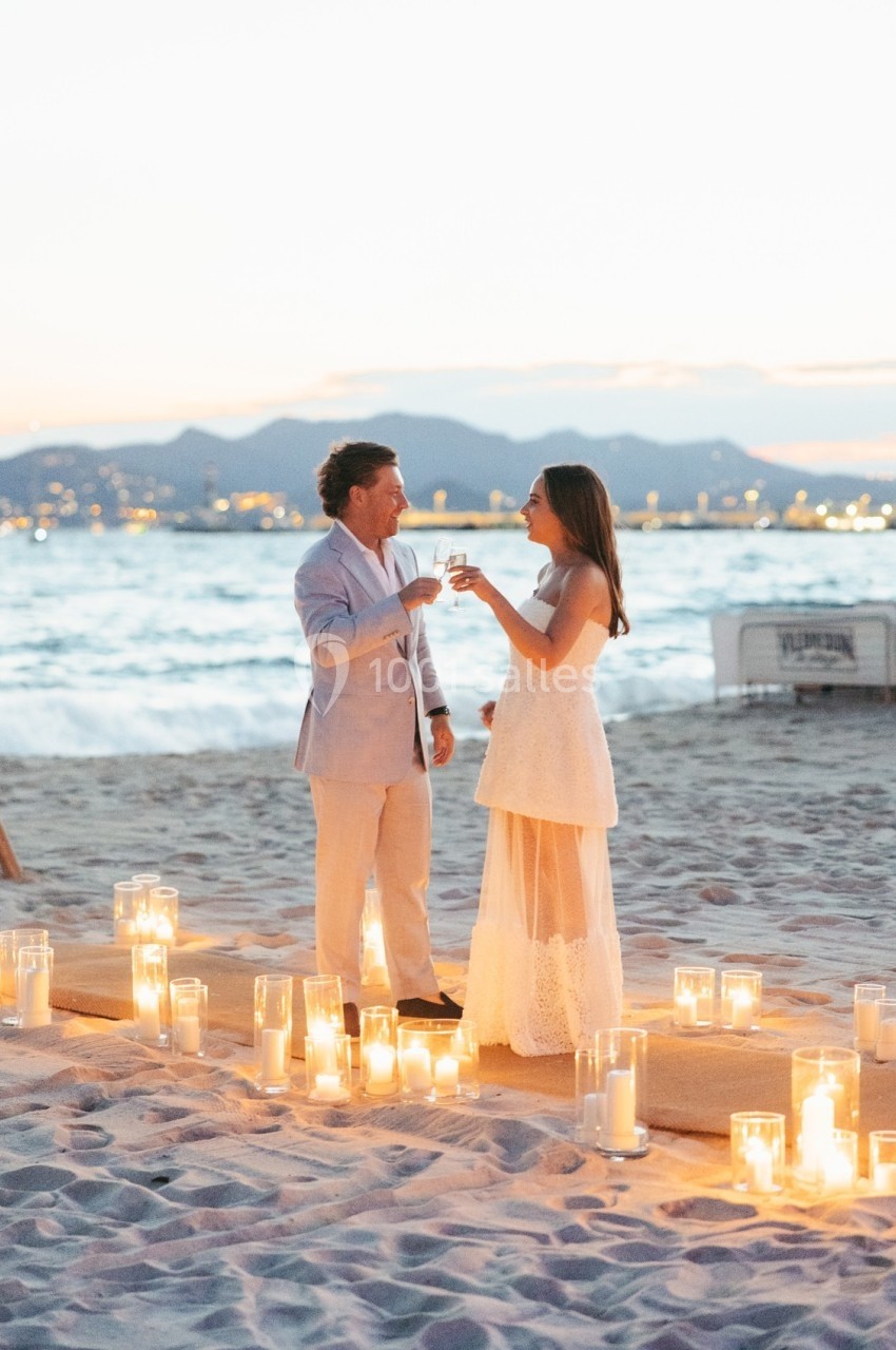 Un couple trinque sur une plage au coucher du soleil, entouré de bougies allumées.