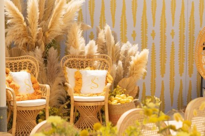 Chaises en rotin entourées de pampas et de décorations jaunes, sous un parasol blanc dans un cadre lumineux.