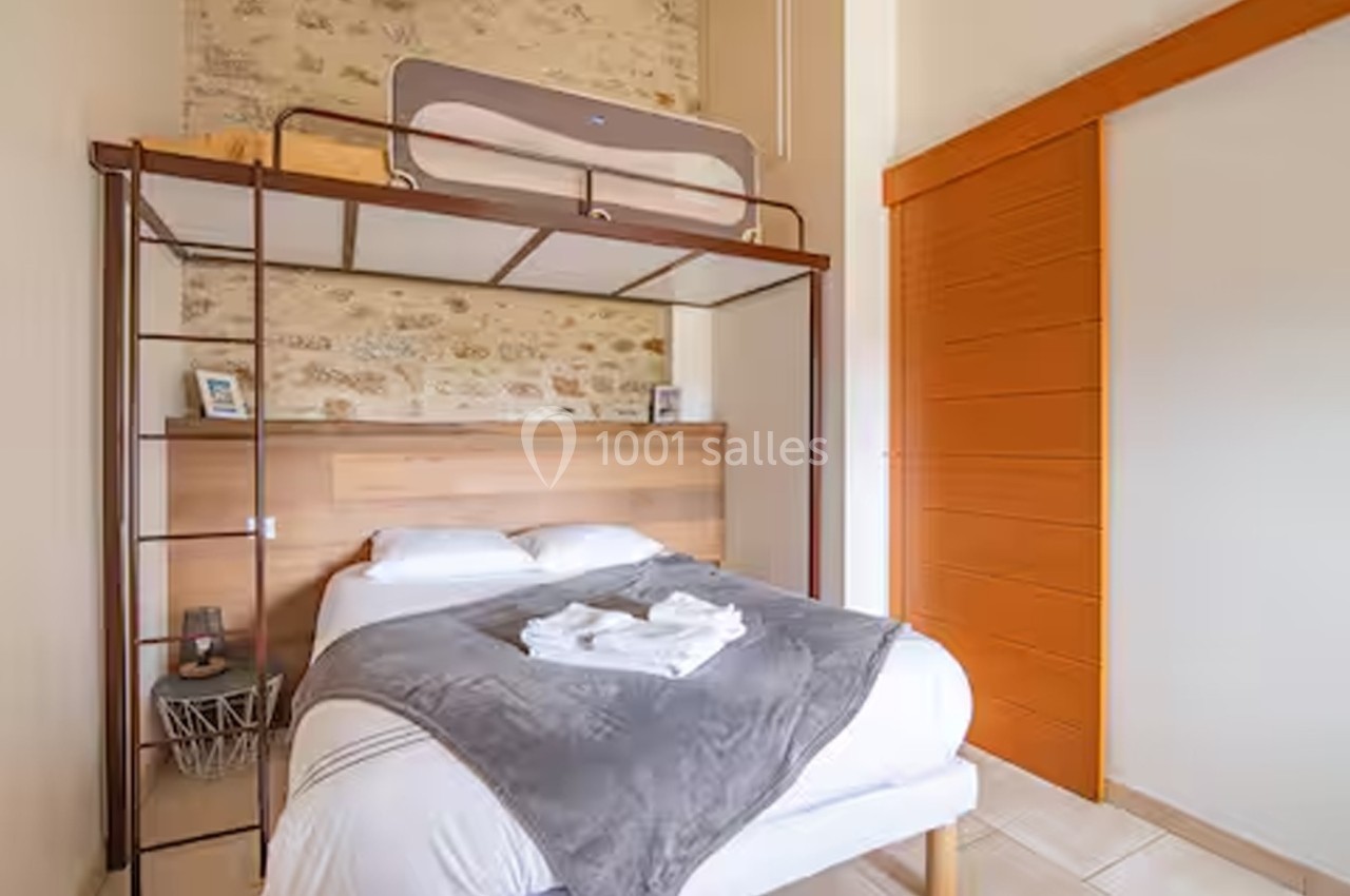 Lit double avec mezzanine en bois, mur en pierre apparente, armoire à porte coulissante orange et linge de lit plié.