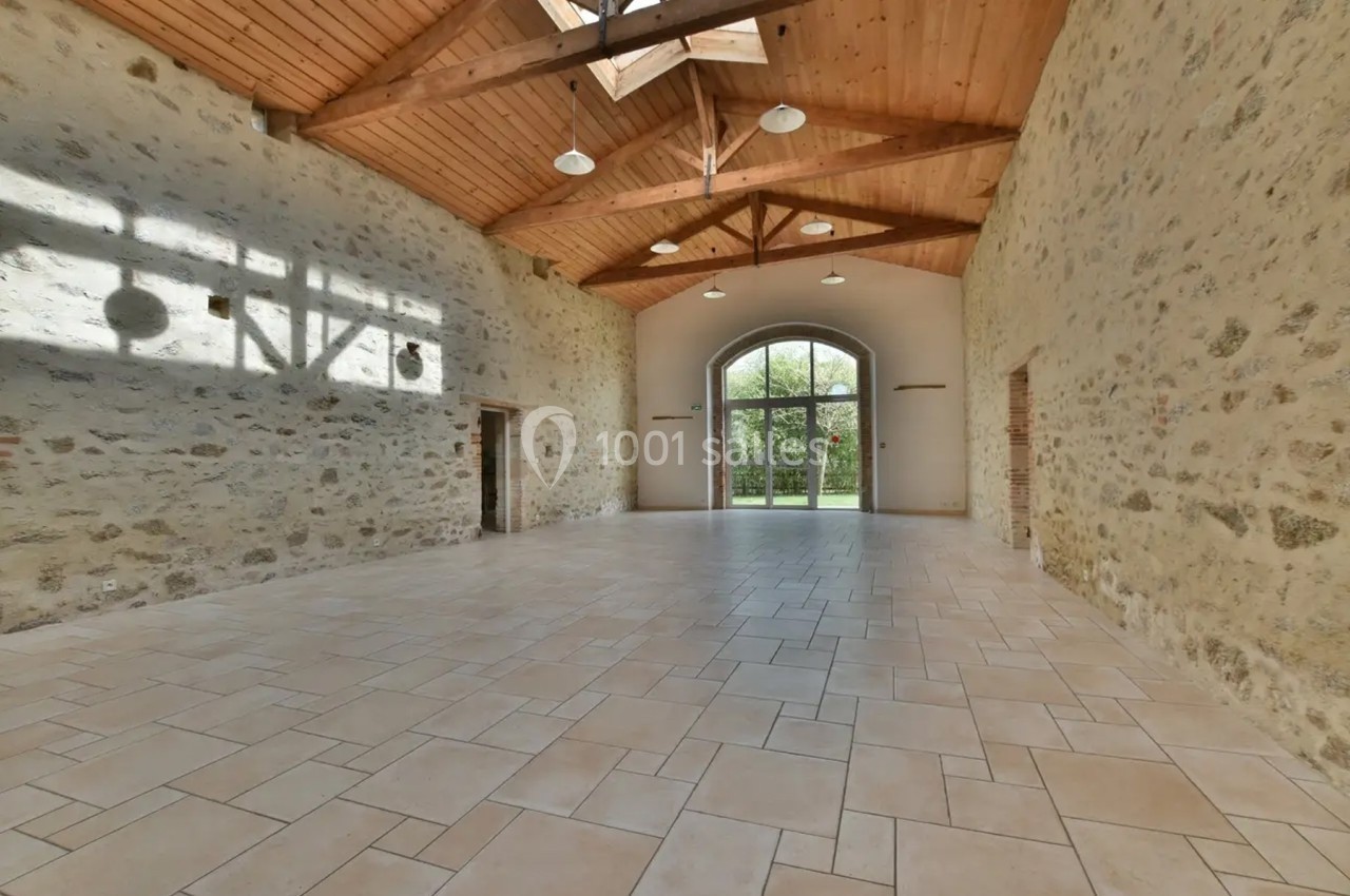 Salle spacieuse avec murs en pierre, plafond en bois et grande baie vitrée donnant sur un jardin.