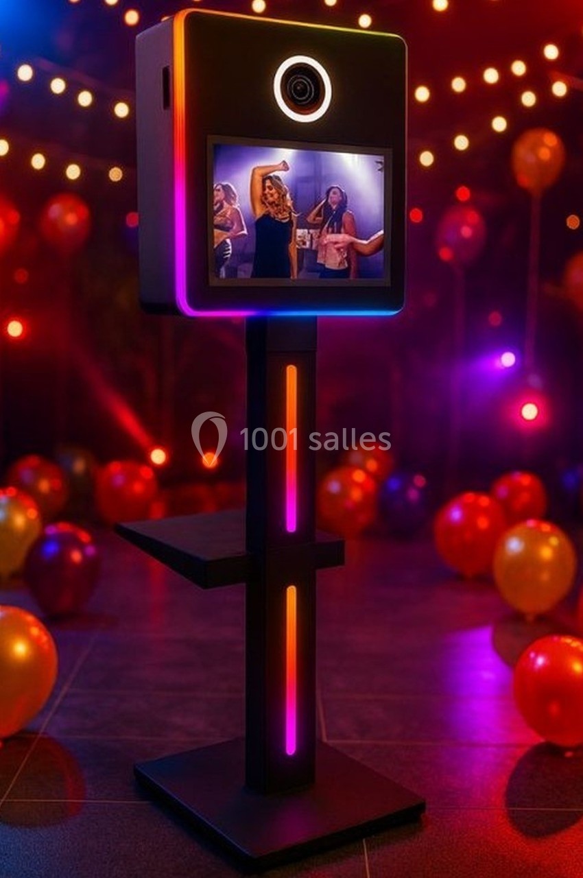 Borne photo lumineuse avec écran affichant des personnes dansant, entourée de ballons et d'éclairages festifs.