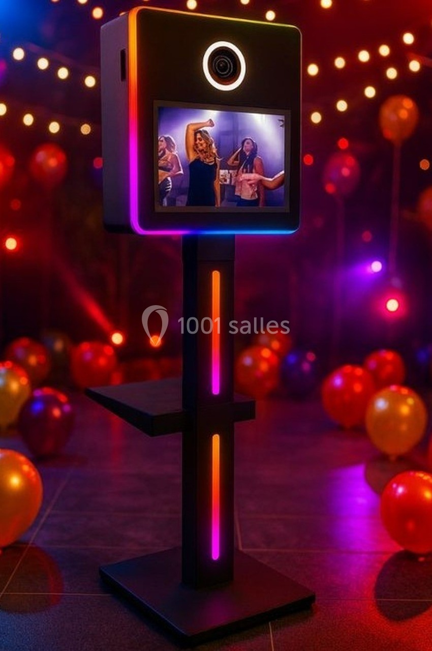 Borne photo lumineuse avec écran affichant des personnes dansant, entourée de ballons et de guirlandes lumineuses.