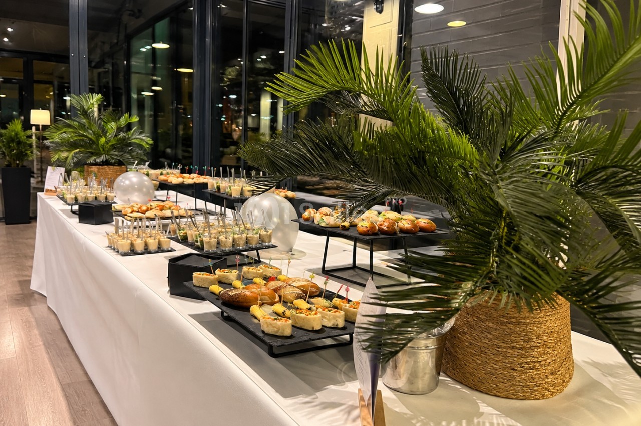 Buffet dressé avec canapés et amuse-bouches sur plateau blanc, plantes vertes et grandes baies vitrées en arrière-plan.