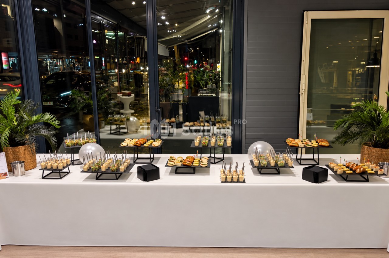 Buffet de canapés et verrines sur table blanche, vitrine ouverte sur rue la nuit en centre-ville.