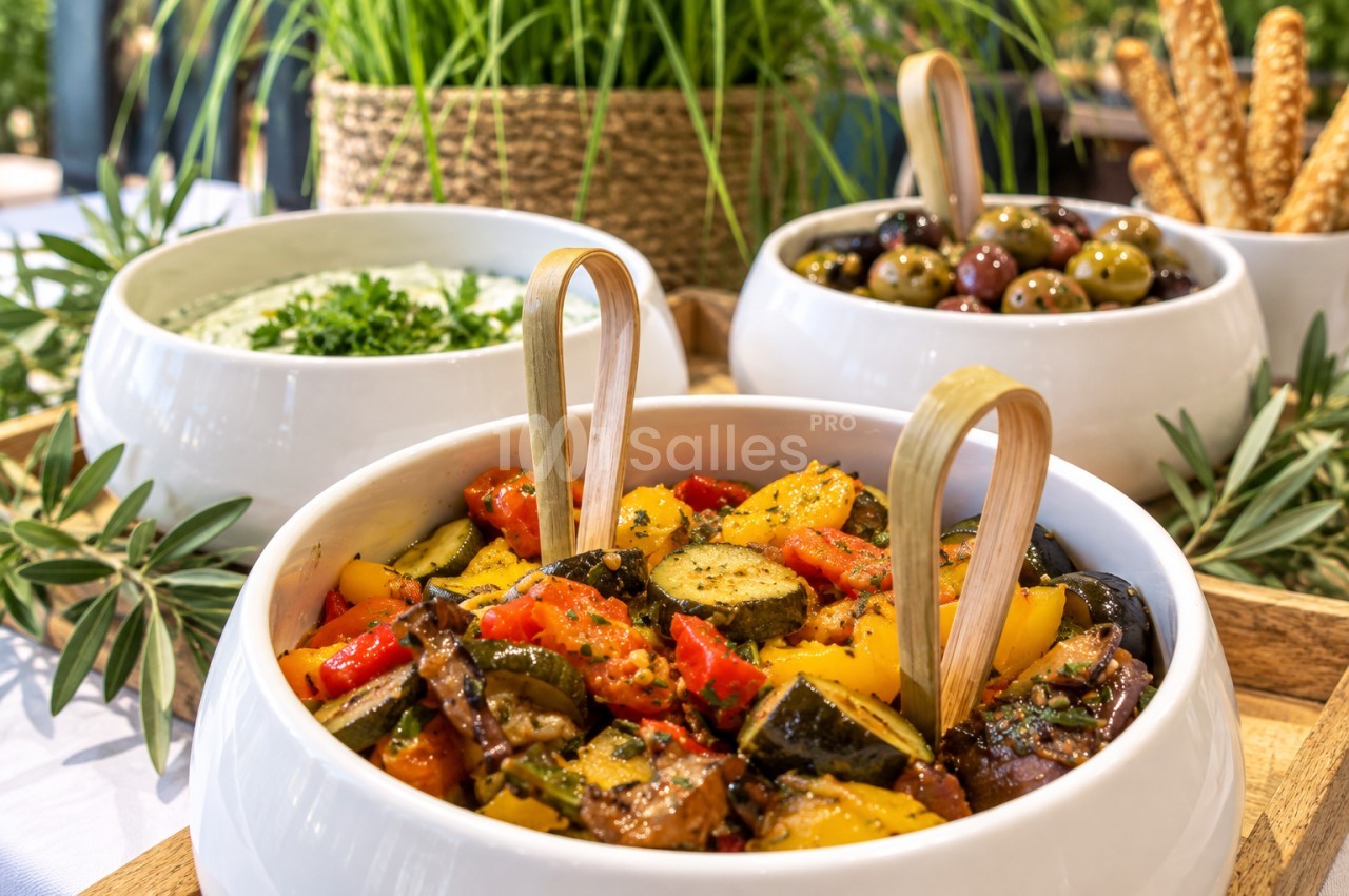 Ratatouille servie en plat collectif entouré de bols d'accompagnements et plantes vertes.