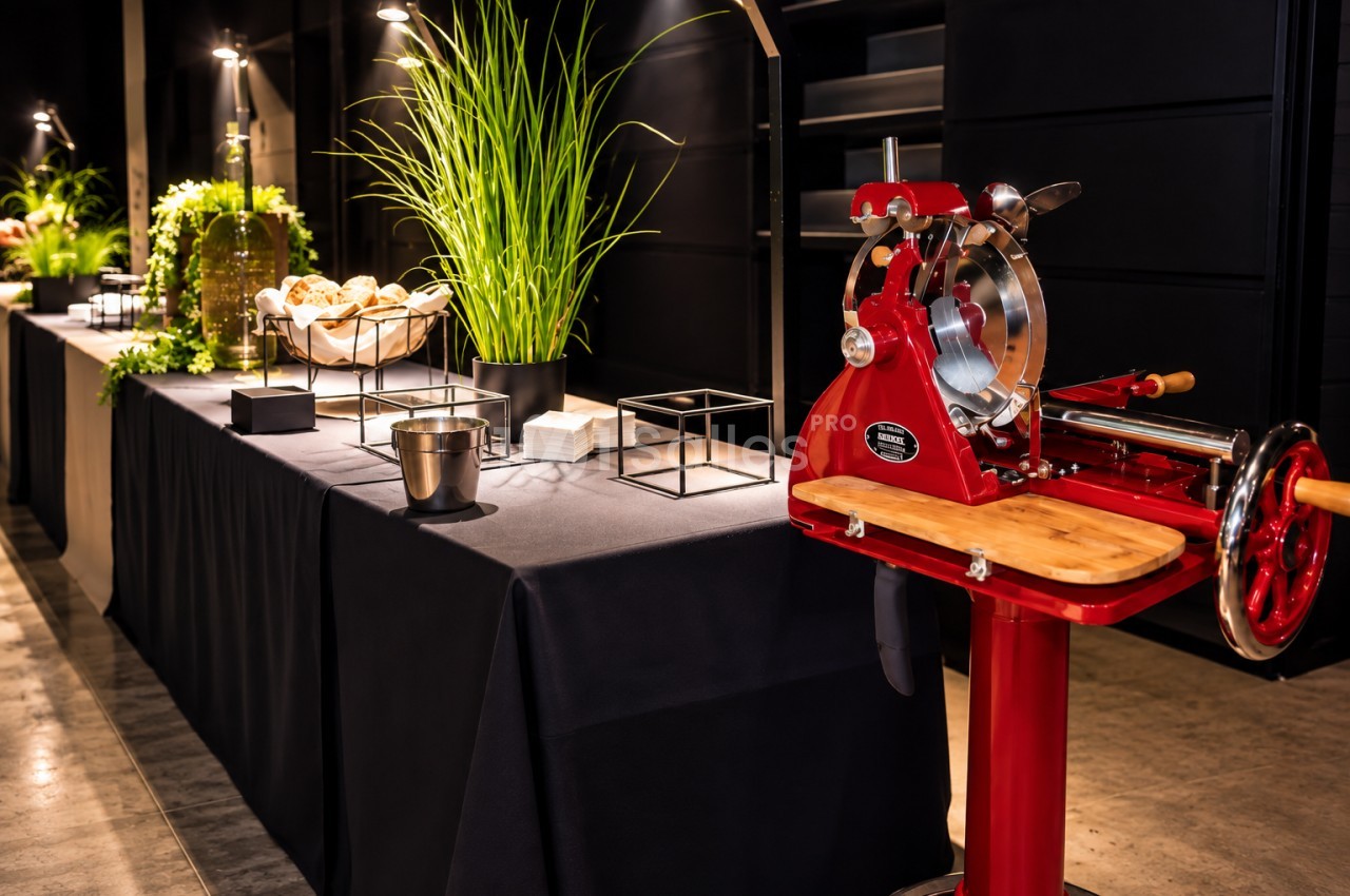 Buffet traiteur avec trancheuse à jambon rouge, pains, plantes et décoration épurée en intérieur.