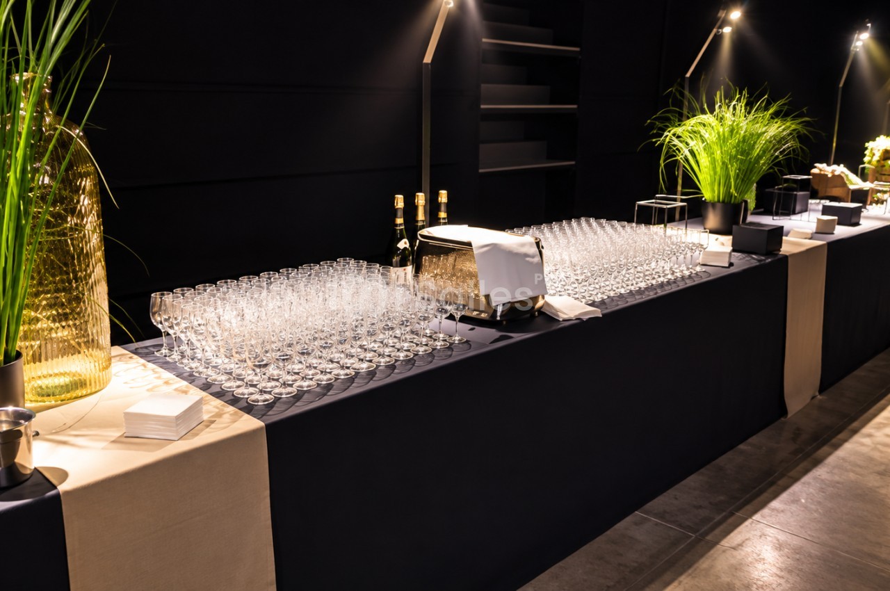 Comptoir de bar de réception nocturne avec verres alignés, bouteilles et plantes vertes éclairées.