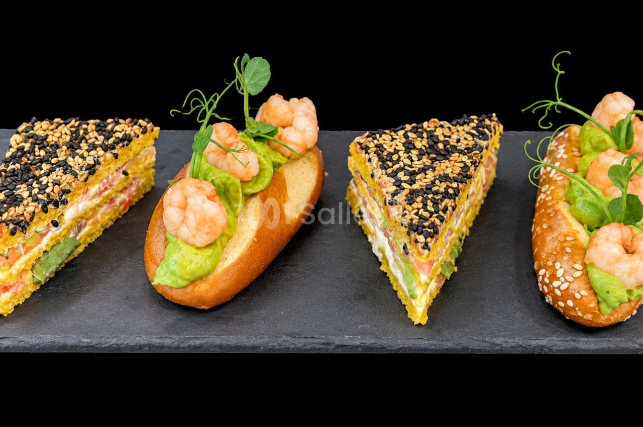 Sélection de canapés gastronomiques - triangles aux graines de sésame et noir, tartines garnies de crevettes et purée d'avocat sur ardoise.