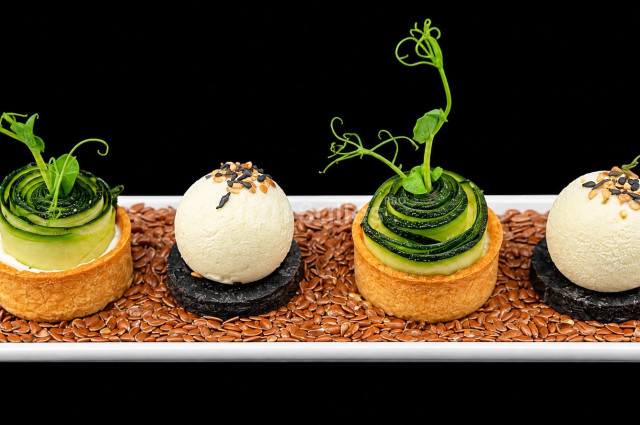 Quatre petits desserts sur lit de graines - deux boules de glace vanille, deux mousses vertes avec plants miniatures et glaçage aux graines.