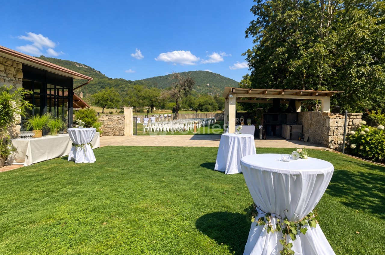 Espace extérieur aménagé pour mariage avec tables rondes drapées en blanc, chaises de cérémonie et montagnes en arrière-plan.