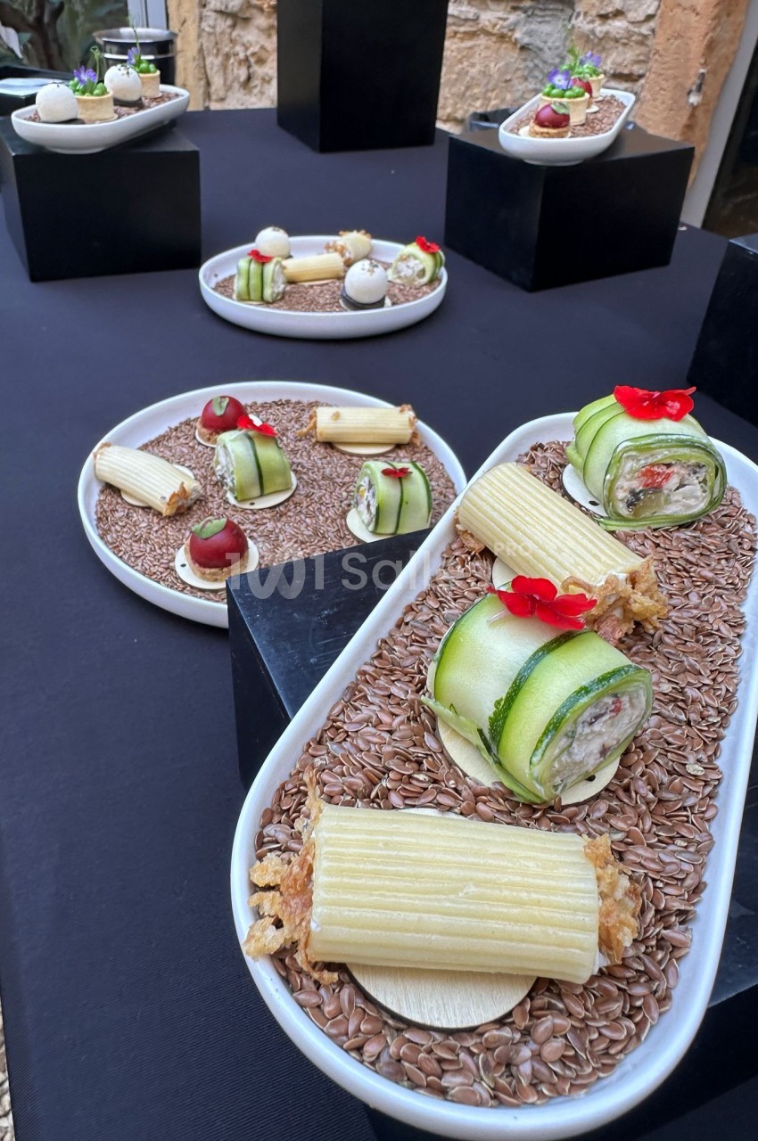 Assiettes de mises en bouche gastronomiques dressées sur table noire - roulés de courgette, terrine, pâtes et décor floral rouge.