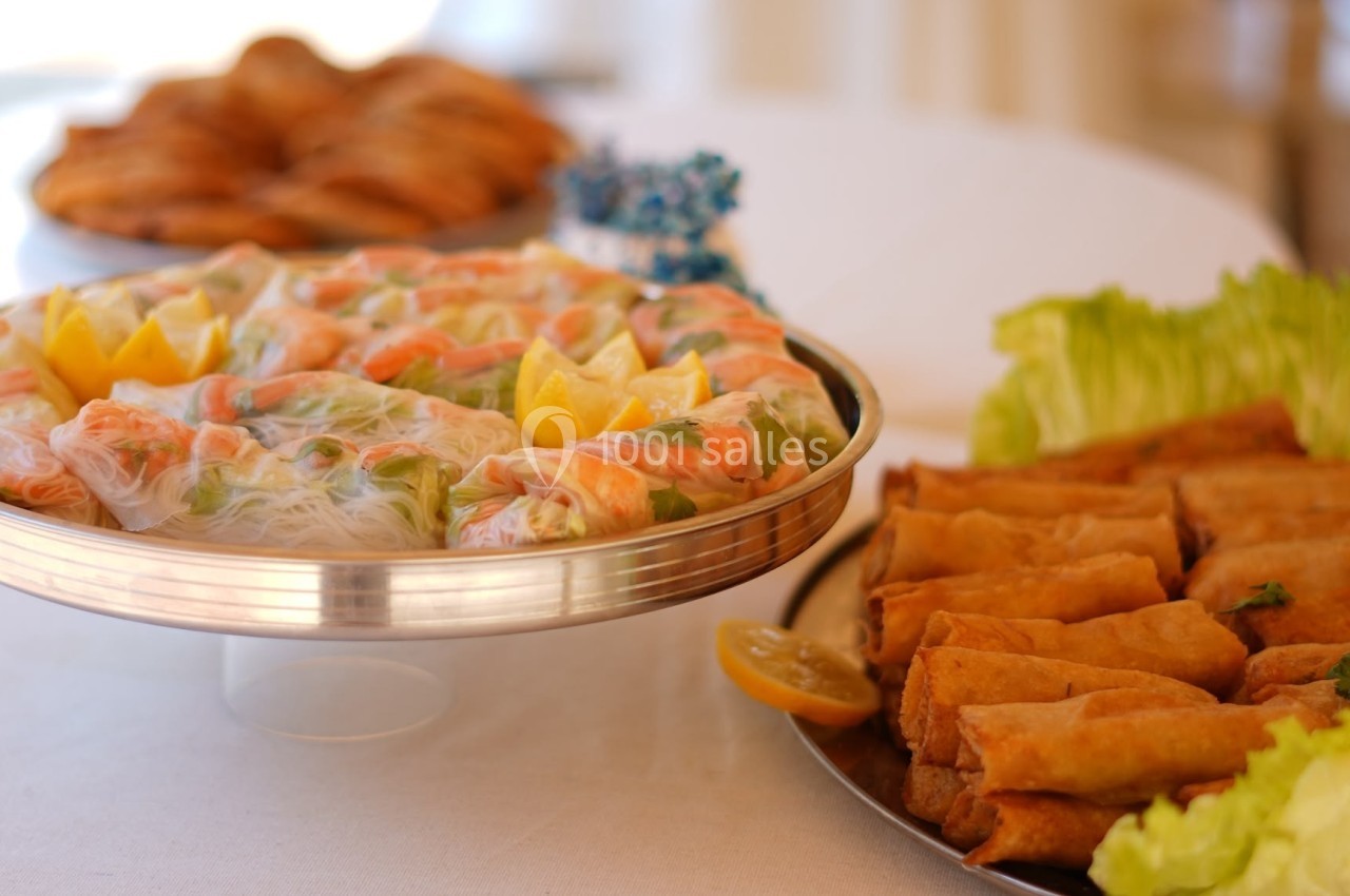 Plateau de rouleaux de printemps aux crevettes et légumes à côté d'un plat de nems, sur une table dressée.