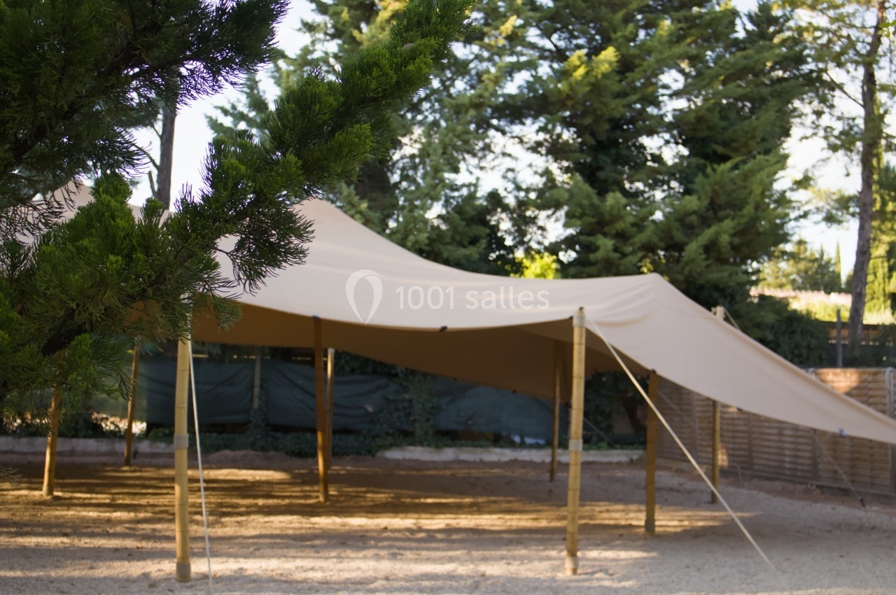 Toile tendue beige montée sur des poteaux en bois, offrant de l'ombre dans un espace extérieur entouré d'arbres.