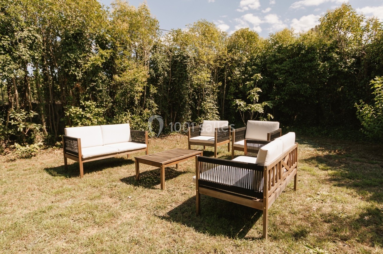 Salon de jardin en bois avec coussins clairs, composé de fauteuils, d'un canapé et d'une table basse, installé sur une…