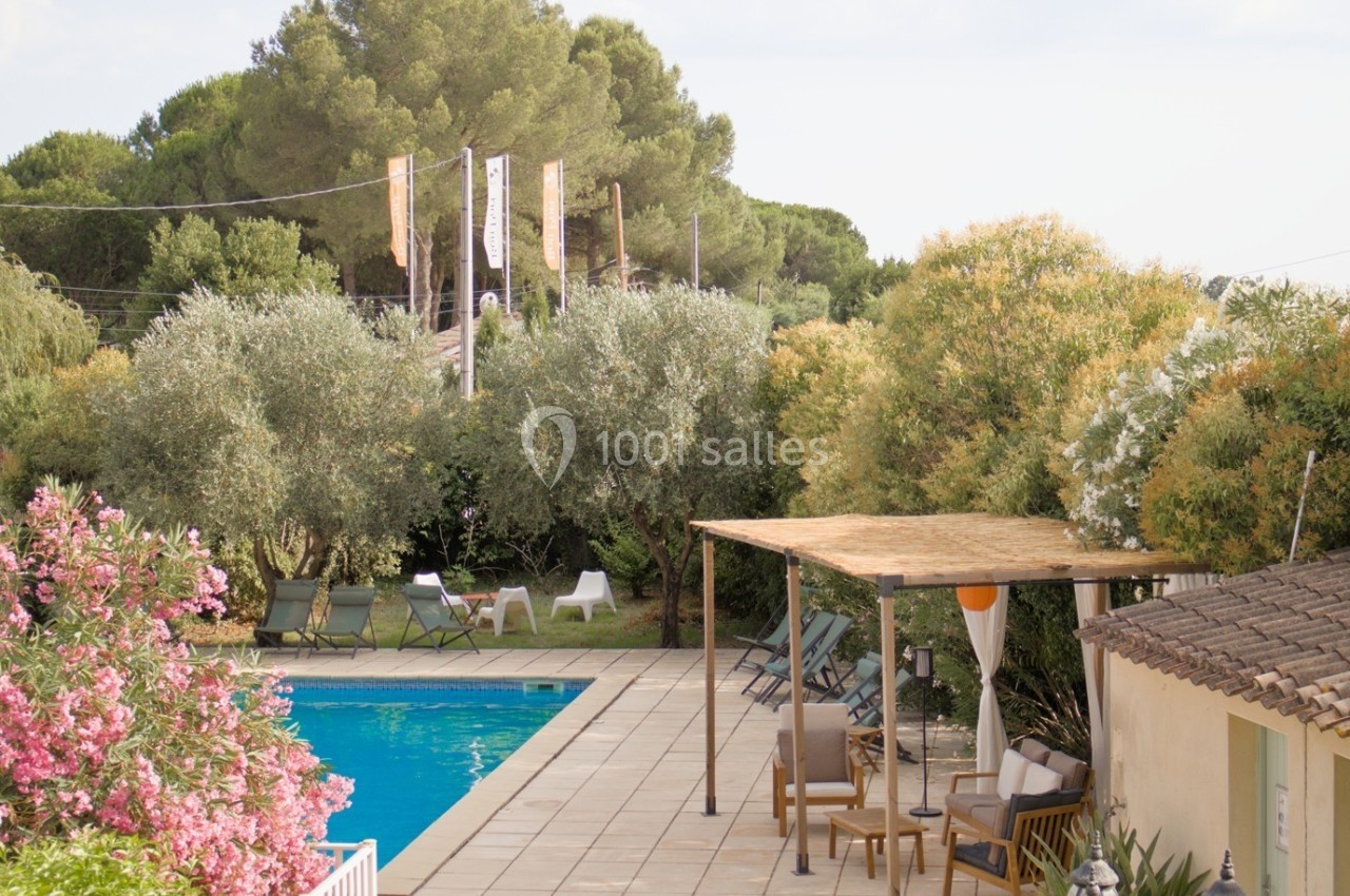 Piscine extérieure entourée de chaises longues, d'arbres et de fleurs, avec une pergola en toile sur la terrasse.