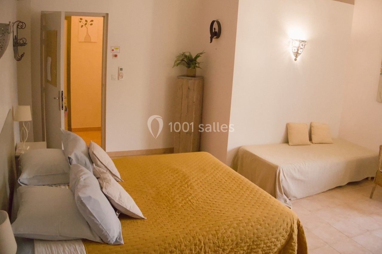 Chambre lumineuse avec lit double, couvre-lit jaune, canapé beige, décor sobre et éclairage mural.