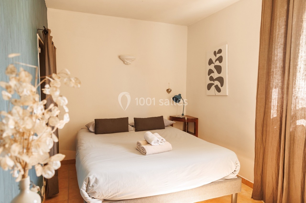 Chambre lumineuse avec lit double, linge plié, lampe de chevet et décoration murale minimaliste.
