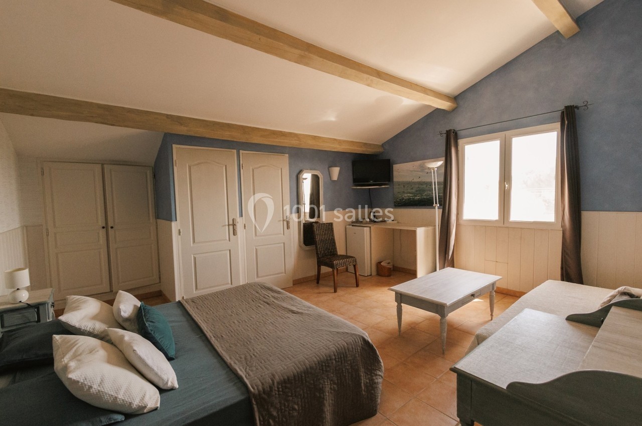 Chambre lumineuse avec lit double, lit simple, armoire, table basse, télévision et fenêtre donnant sur l'extérieur.