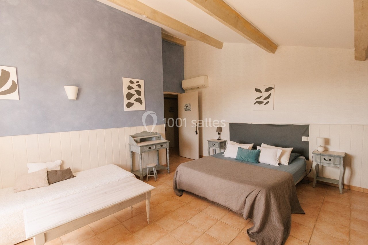 Chambre lumineuse avec lit double, lit simple, murs clairs, poutres apparentes et mobilier en bois peint.
