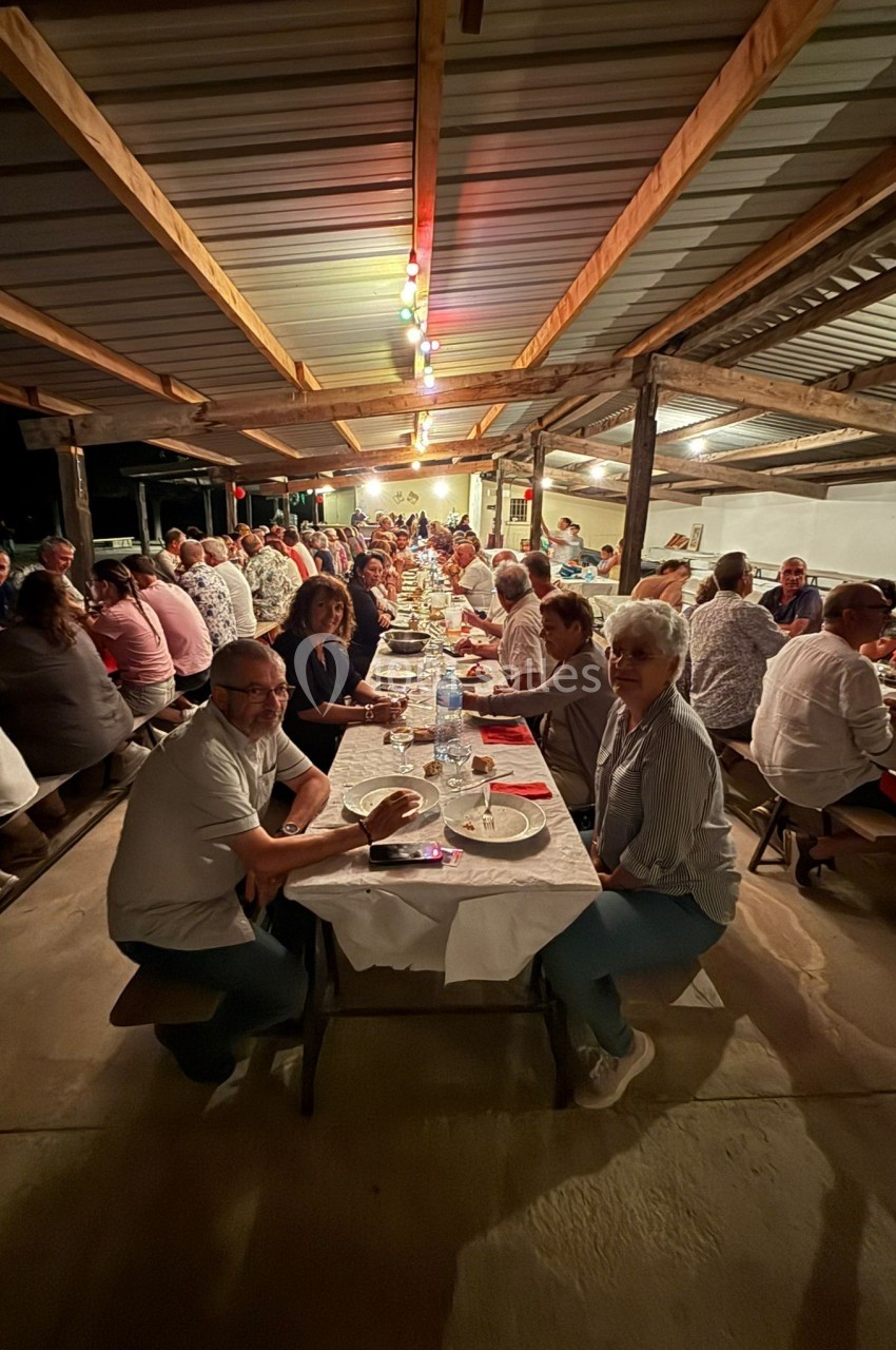 Des personnes assises à de longues tables sous un abri éclairé, partageant un repas convivial en soirée.