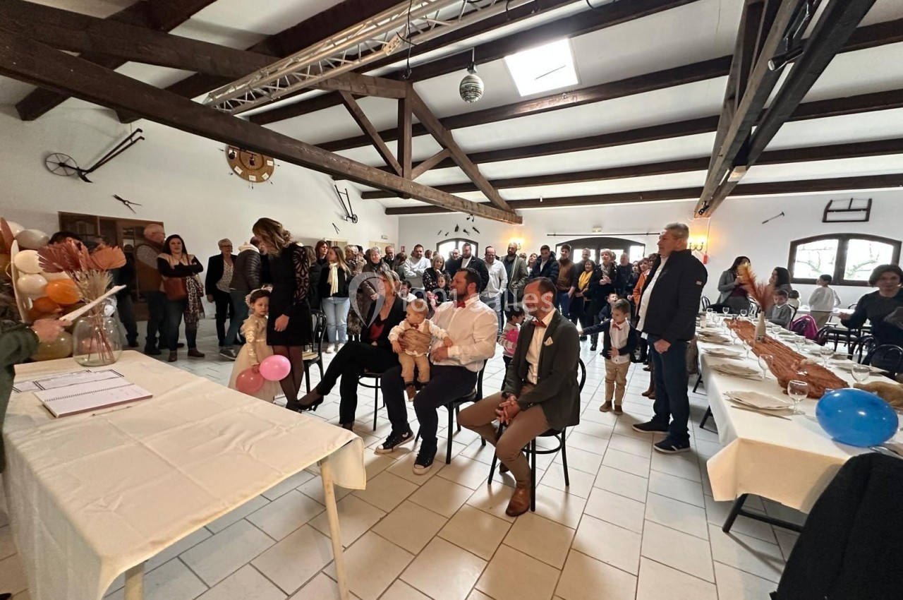 Groupe de personnes rassemblées dans une salle lumineuse avec poutres apparentes, lors d'un événement festif.