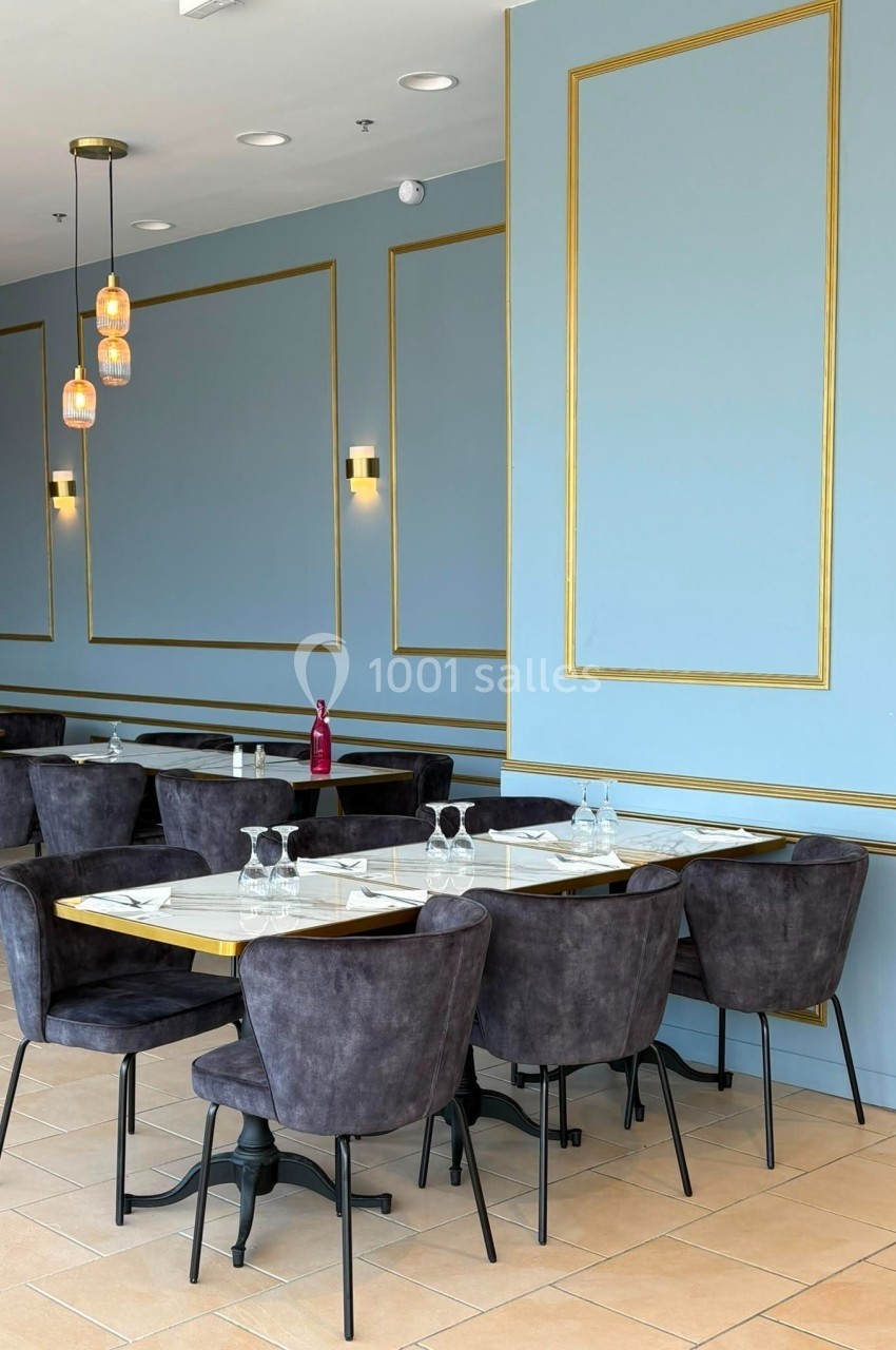 Salle de restaurant élégante avec murs bleus et dorés, tables dressées et chaises en velours gris.