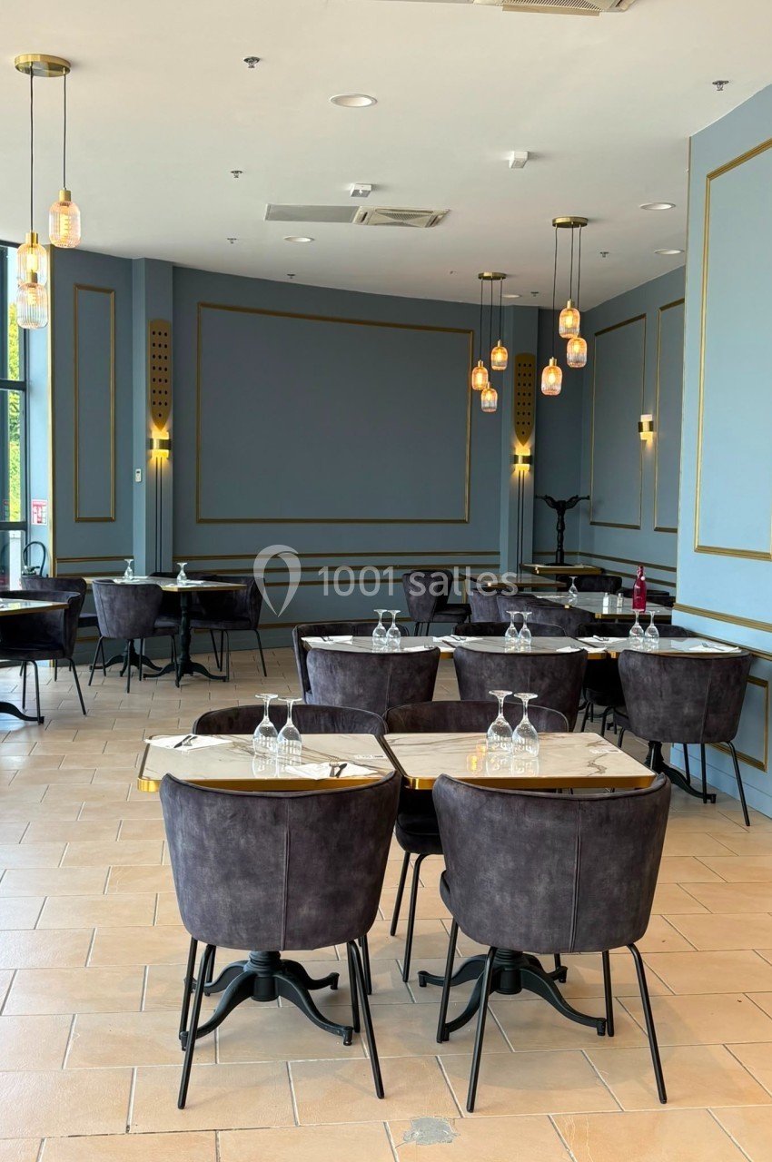Salle de restaurant élégante avec des tables en marbre, chaises noires et luminaires suspendus dans un décor bleu et doré.