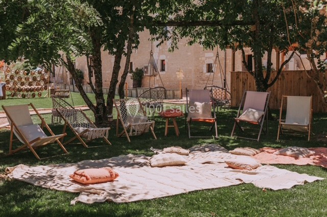 Chaises longues et coussins disposés sur une pelouse ombragée, entourés d'arbres et d'une ambiance extérieure paisible.