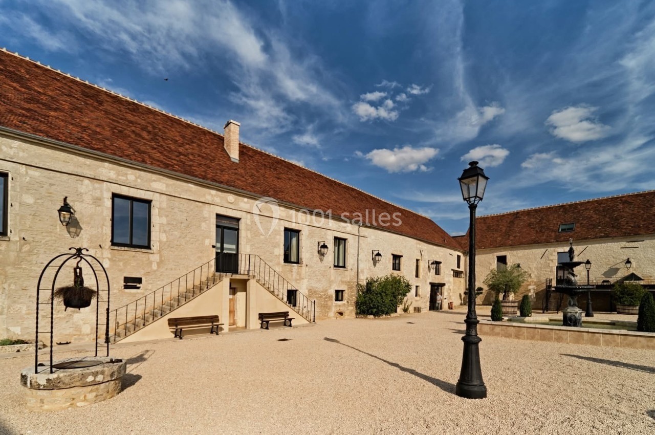 Cour intérieure d'un bâtiment en pierre avec toit en tuiles, lampadaire, puits et ciel dégagé en arrière-plan.