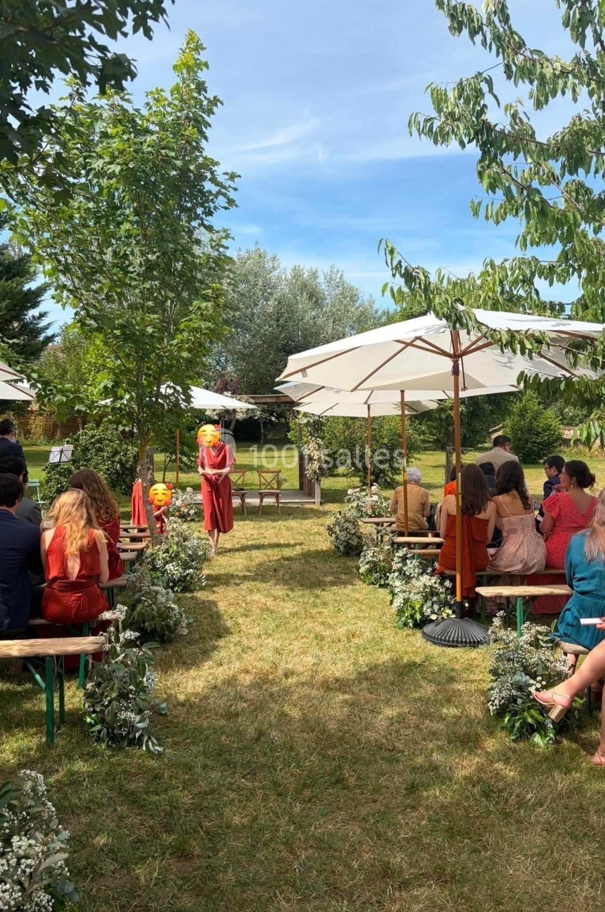 Invités assis sous des parasols lors d'une cérémonie en plein air, entourés de verdure et de décorations florales.
