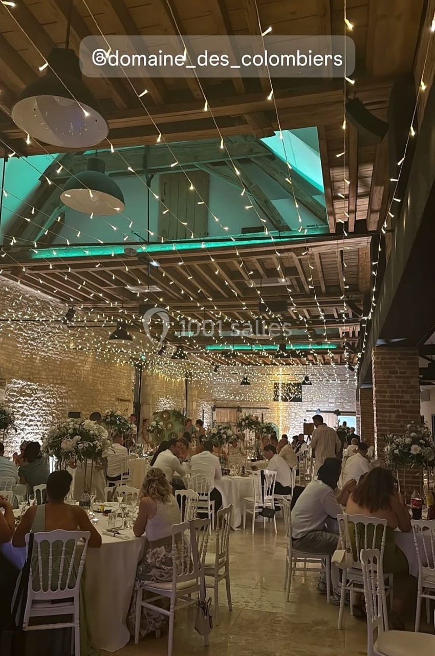 Salle de réception décorée de guirlandes lumineuses suspendues, avec des invités assis à des tables rondes.