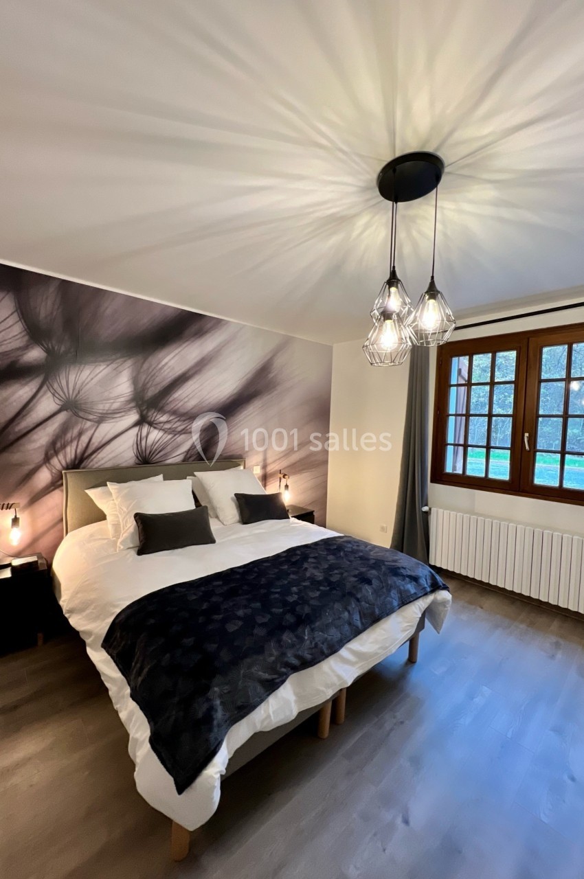 Chambre lumineuse avec un lit double, une décoration murale artistique, des lampes suspendues et une grande fenêtre.