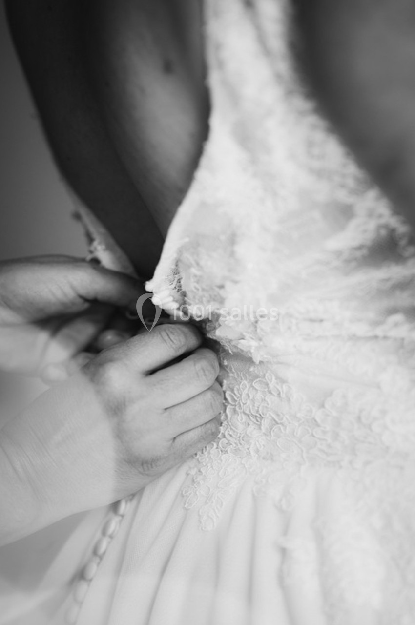 Main ajustant les boutons d'une robe de mariée en dentelle dans un plan rapproché en noir et blanc.