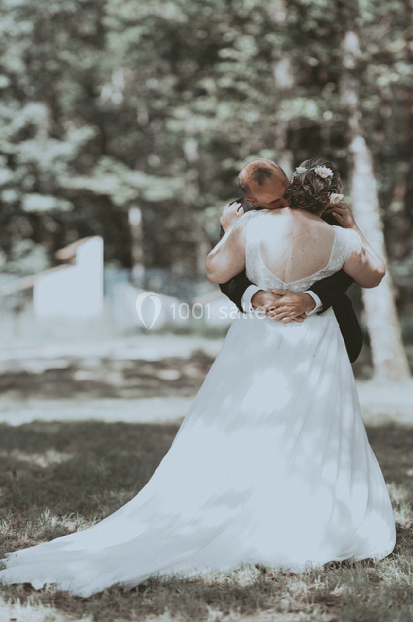 Un couple de mariés s'enlace dans un jardin ombragé, la mariée portant une robe blanche avec un dos ouvert.