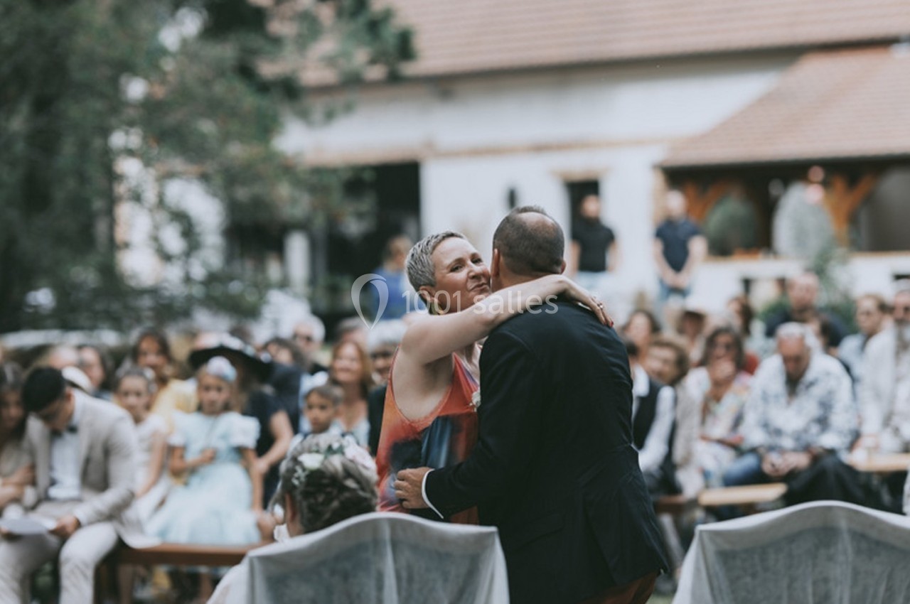 Un couple s'enlace lors d'une cérémonie en plein air, entouré d'invités assis dans un jardin.