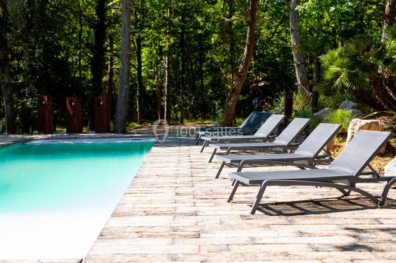 Chaises longues alignées au bord d'une piscine entourée de végétation et d'arbres dans un cadre ensoleillé.