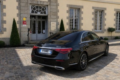 Deux véhicules Mercedes noirs stationnés sur un sol pavé devant un bâtiment en pierre sous un ciel nuageux.