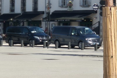 Deux véhicules Mercedes noirs stationnés sur un sol pavé devant un bâtiment en pierre sous un ciel nuageux.