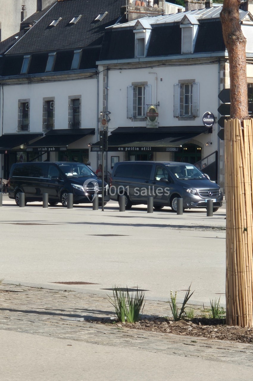 Deux vans noirs stationnés devant des bâtiments avec façades blanches et commerces au rez-de-chaussée.
