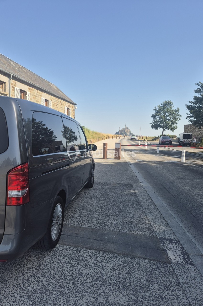 Un van gris stationné sur une route menant au Mont-Saint-Michel visible au loin par temps clair.
