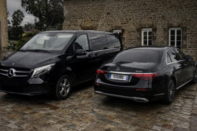 Deux véhicules Mercedes noirs stationnés sur un sol pavé devant un bâtiment en pierre sous un ciel nuageux.