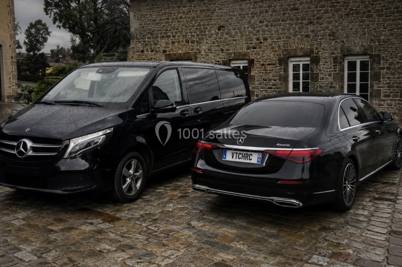 Deux véhicules Mercedes noirs stationnés sur un sol pavé devant un bâtiment en pierre sous un ciel nuageux.