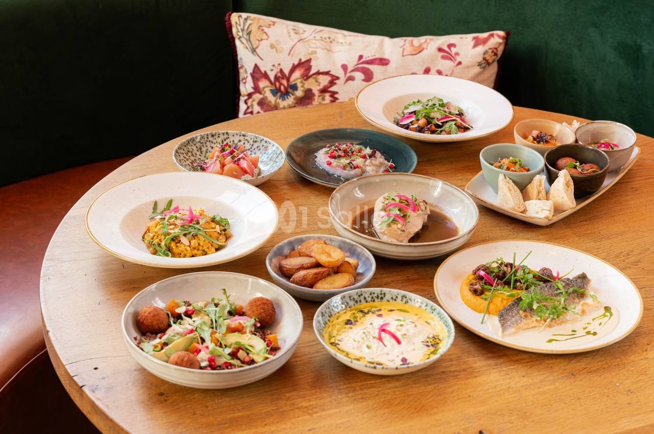 Plusieurs plats gastronomiques dressés sur une table en bois - poisson, croquettes, salade, œuf et légumes - fond vert.