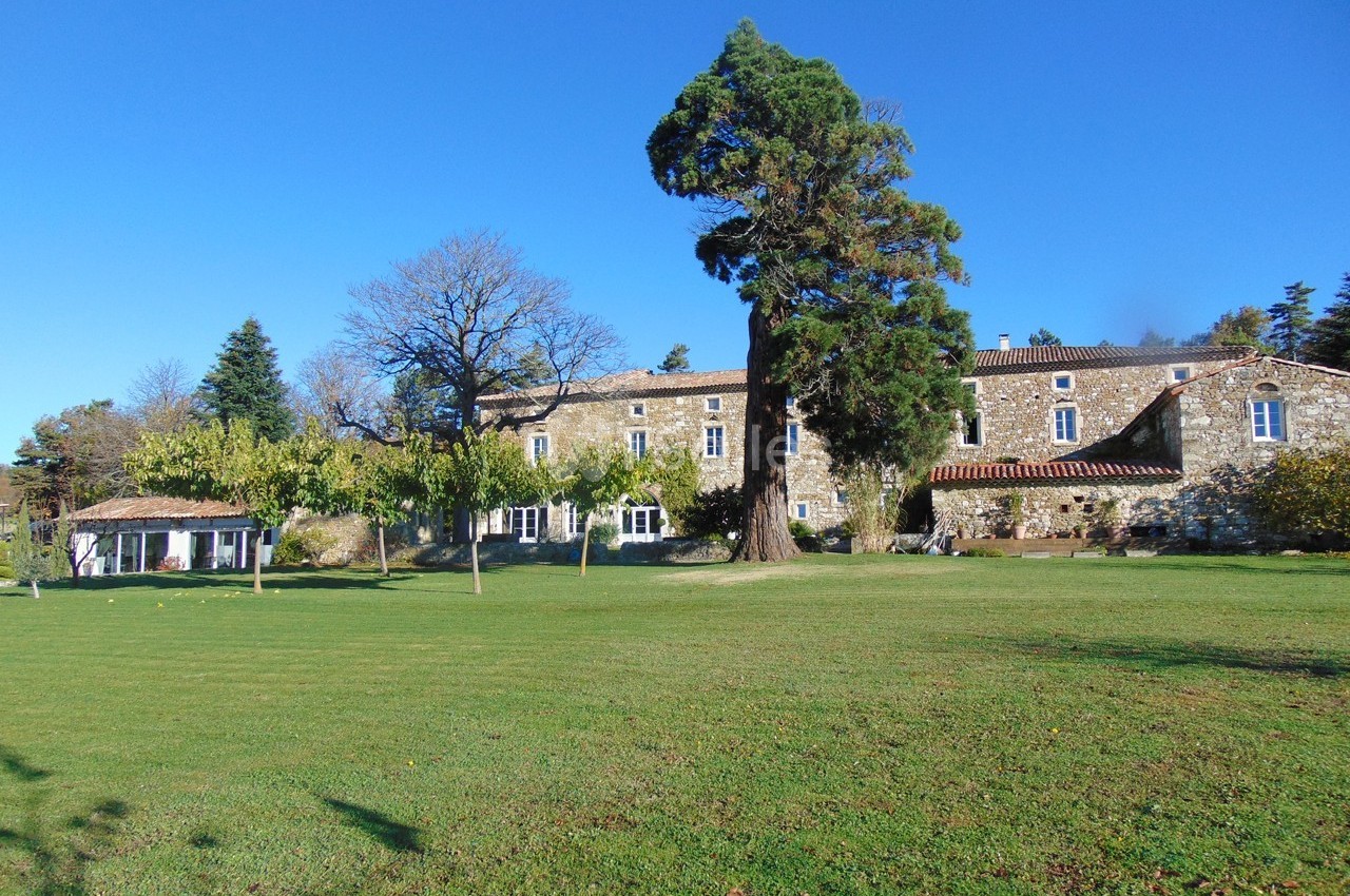 Bâtisse en pierre entourée d'arbres et d'une pelouse verdoyante sous un ciel bleu dégagé.