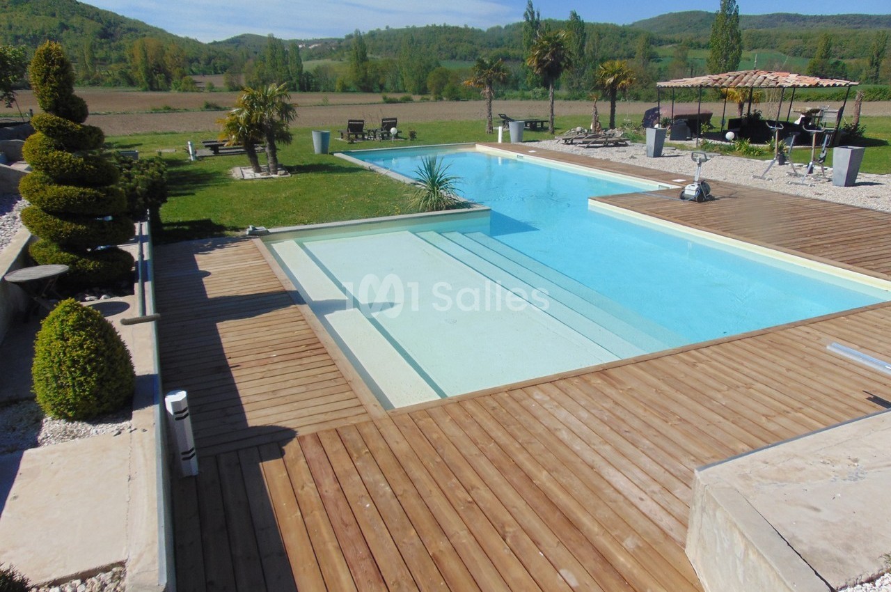 Piscine extérieure avec terrasse en bois, entourée de végétation et offrant une vue sur un paysage rural.
