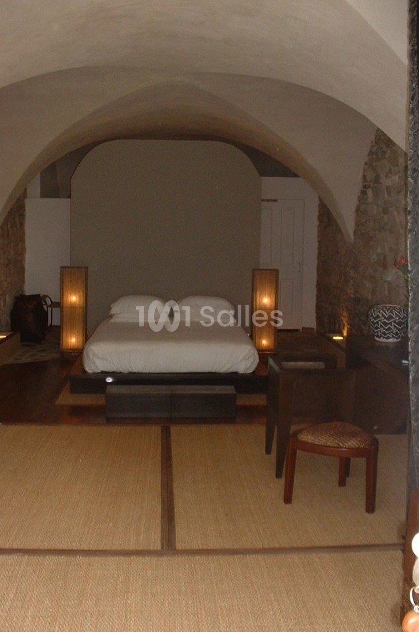 Chambre avec voûtes en pierre, lit double, éclairage tamisé et sol en tatami dans un décor minimaliste.