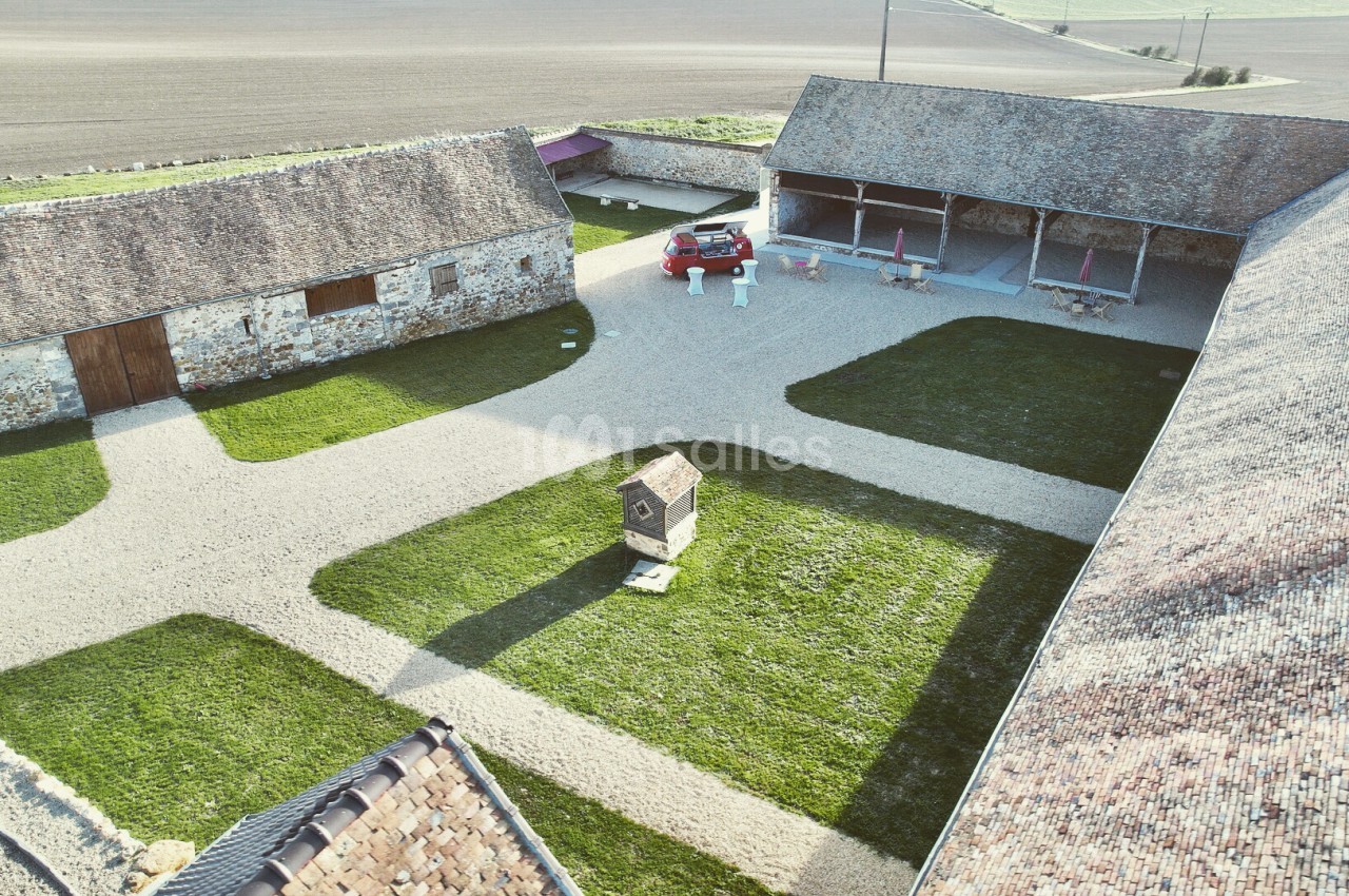 Cour de ferme avec bâtiments en pierre, allées gravillonnées, pelouses et voiture garée.